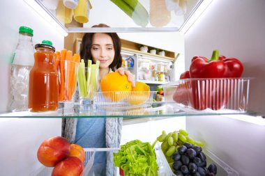Sağlıklı yiyecek, sebze ve meyvelerle dolu açık buzdolabının yanında duran kadın portresi. Kadın portresi