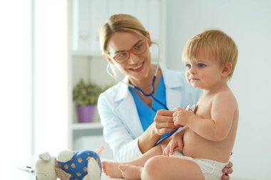 Kadın doktor, klinikte steteskoplu bir çocuğu dinliyor.
