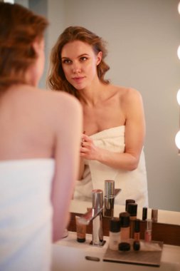 Genç bir kadın aynaya bakıyor ve makyaj yapıyor..