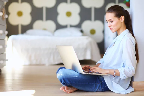 Ung kvinna som sitter på golvet nära barnens babysäng med laptop. Ung mamma — Stockfoto