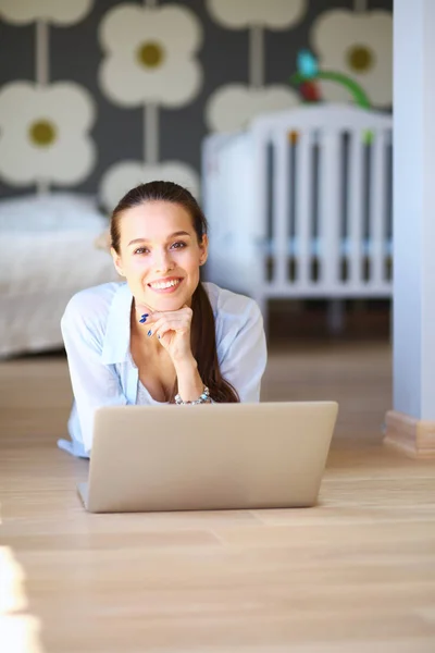 Jonge vrouw zittend op de vloer in de buurt van childrens kinderbed met laptop. Jonge moeder — Stockfoto