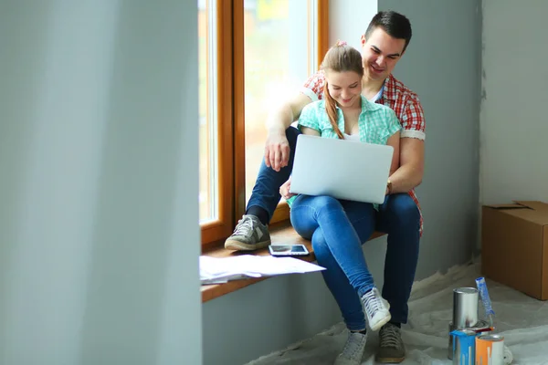 Retrato de pareja joven moviéndose en casa nueva sentado con el ordenador portátil —  Fotos de Stock