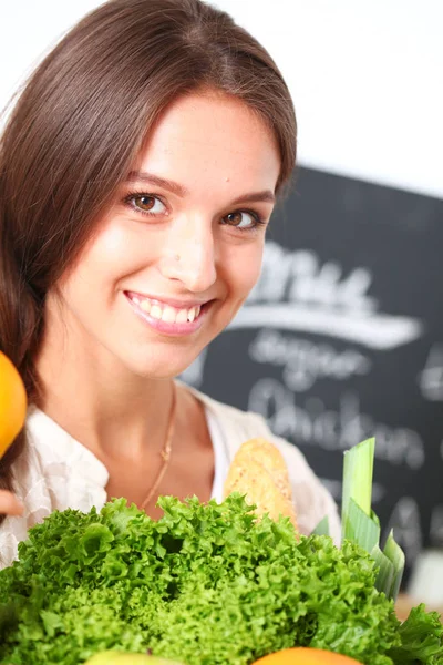 Smiling young woman holding vegetables standing in kitchen. Smiling young woman — Stock Photo, Image