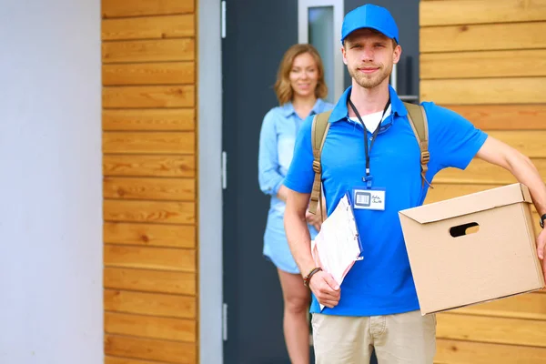 Lächelnder Zusteller in blauer Uniform liefert Paketkasten an Empfänger aus - Kurierdienst-Konzept. Lächelnder Zusteller in blauer Uniform — Stockfoto