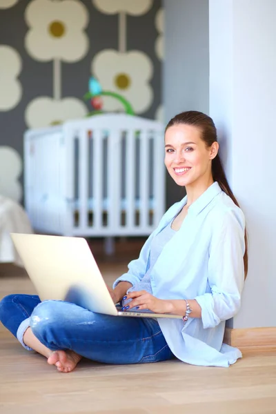 Young woman sitting on the floor near childrens cot with laptop. Young mom — Stock Photo, Image