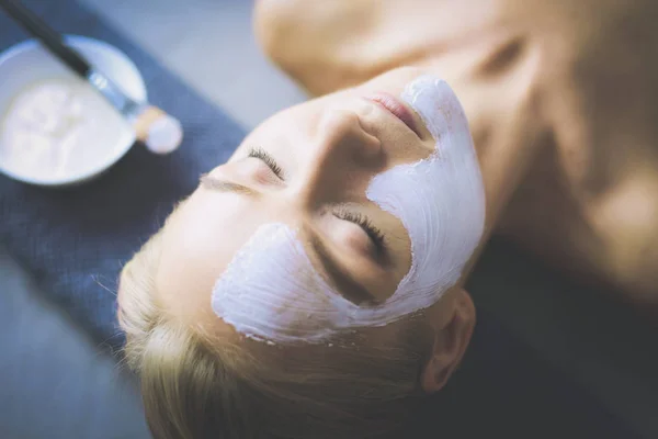 Gezichtsmasker. Mooi jong meisje in spa, schoonheidsspecialist vrouw gezicht masker toe te passen. — Stockfoto