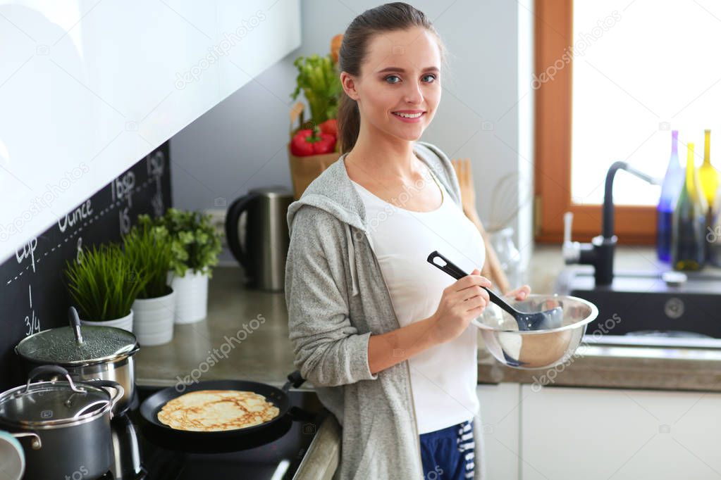 Young woman prepares pancakes in the kitchen while standing near the table. Woman in the kitchen. Cooking at kitchen.