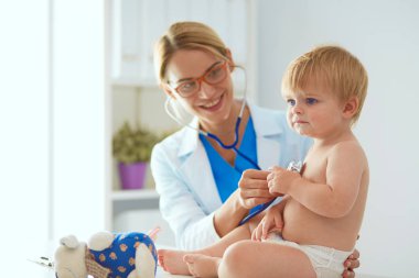 Kadın doktor, klinikte steteskoplu bir çocuğu dinliyor.