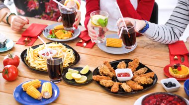 Ahşap masada otururken birlikte yemek yiyen bir grup insanın üst düzey görüntüsü. Masada yemek var. İnsanlar fast food yiyor..