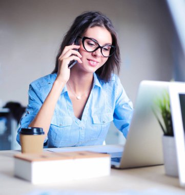 Ofis masasında oturan ve cep telefonuyla konuşan genç ve güzel bir iş kadını. İş kadını