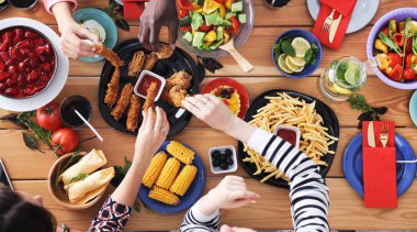 Ahşap masada otururken birlikte yemek yiyen bir grup insanın üst düzey görüntüsü. Masada yemek var. İnsanlar fast food yiyor..