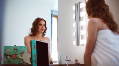 Genç bir kadın aynaya bakıyor ve makyaj yapıyor.