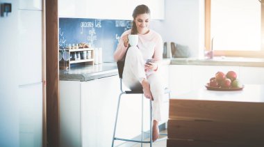 modern mutfakta otururken cep telefonu kullanan kadın