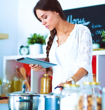 Mutfakta yemek yapmak için tablet bilgisayar kullanan genç bir kadın.