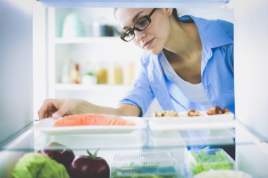 Sağlıklı yiyecek, sebze ve meyvelerle dolu açık buzdolabının yanında duran kadın portresi. Kadın portresi.