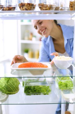 Sağlıklı yiyecek, sebze ve meyvelerle dolu açık buzdolabının yanında duran kadın portresi. Kadın portresi