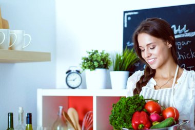 Mutfakta elinde sebzelerle gülümseyen genç bir kadın. Gülümseyen genç kadın