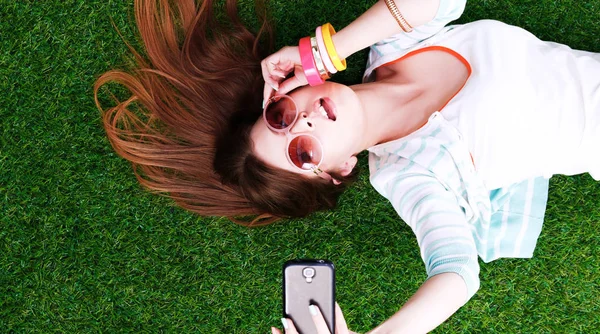 Lachende jonge vrouw liggend op het gras en het maken van een selfie — Stockfoto
