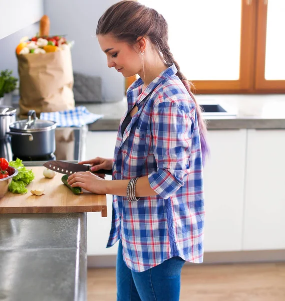 Jonge vrouw snijden van groenten in de keuken in de buurt van bureau. — Stockfoto