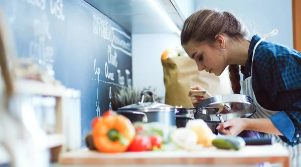 Ung kvinna matlagning i sitt kök står nära spis — Stockfoto