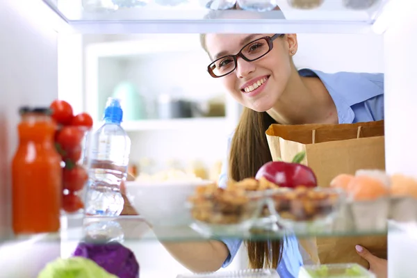 Porträt einer Frau, die neben einem offenen Kühlschrank voller gesunder Lebensmittel, Gemüse und Obst steht. Porträt einer Frau — Stockfoto