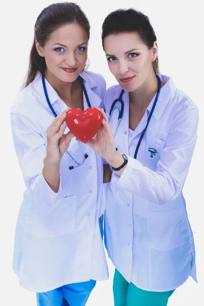 Beyaz arka plan üzerinde izole kırmızı bir kalp tutan iki kadın doktor. İki kadın doktor — Stok fotoğraf