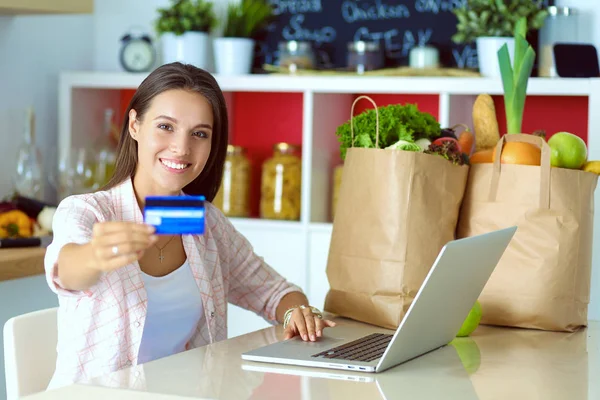 Усміхнена жінка в Інтернеті купує за допомогою планшета та кредитної картки на кухні. Усміхнена жінка — стокове фото