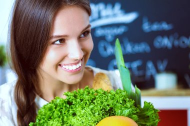 Mutfakta elinde sebzelerle gülümseyen genç bir kadın. Gülümseyen genç kadın