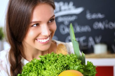 Mutfakta elinde sebzelerle gülümseyen genç bir kadın. Gülümseyen genç kadın