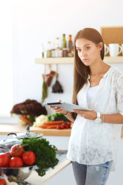 Mutfağında yemek için bir tablet bilgisayar kullanan genç kadın. Genç kadın
