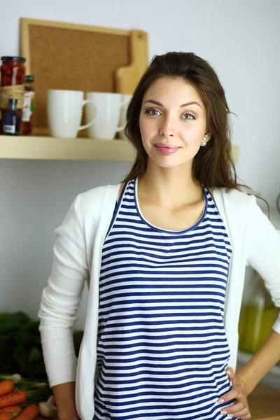 Leende ung kvinna med grönsaker stående i köket. Leende ung kvinna — Stockfoto