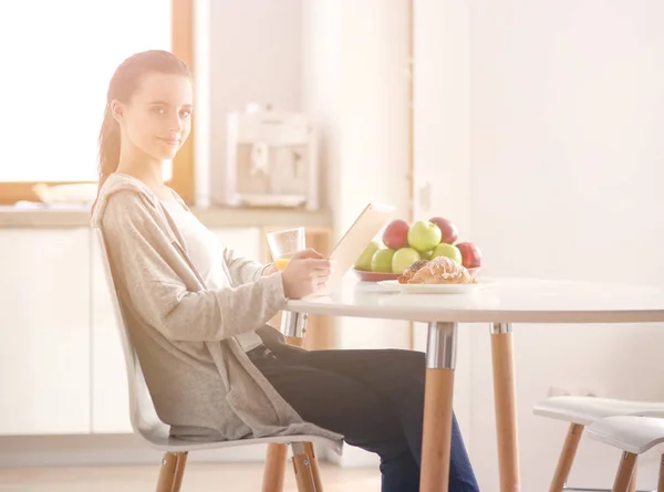 Ung kvinna med apelsinjuice och tablett i köket. — Stockfoto