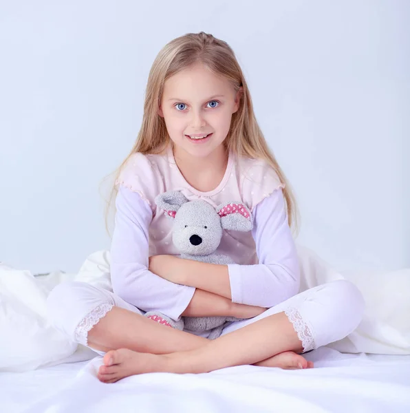 Das kleine Mädchen im Schlafzimmer sitzt auf dem Bett. kleines Mädchen trägt Schlafanzug und sitzt im Bett — Stockfoto