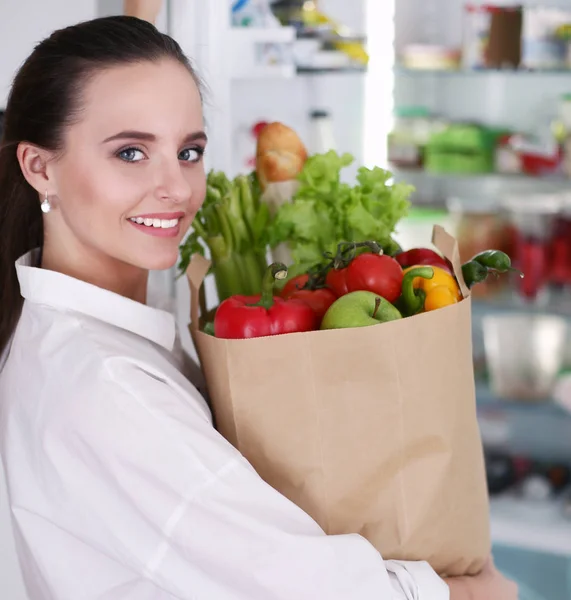Junge Frau hält Einkaufstasche mit Gemüse in der Hand. Frau in der Küche blickt in die Kamera — Stockfoto