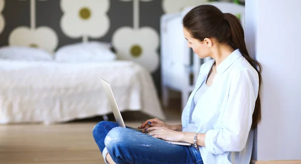 Ung kvinna som sitter på golvet nära barnens babysäng med laptop. Ung mamma — Stockfoto