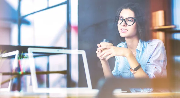 Young woman sitting at office table with laptop,view through window. Young woman — Stock Photo, Image