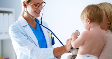 Kadın doktor, klinikte steteskoplu bir çocuğu dinliyor.