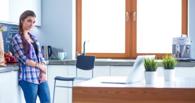 Kollarını mutfak arka planında kavuşturmuş genç bir kadının portresi.