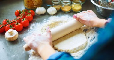 Güzel bir kadın mutfakta pasta pişiriyor. Masanın yanında duruyor.