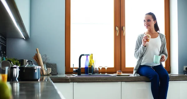 Junge Frau mit Tasse und Kuchen sitzt in Küche — Stockfoto