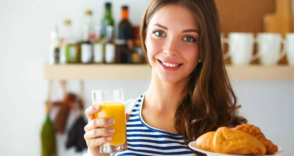 Mujer joven con vaso de jugo y pasteles de pie en la cocina —  Fotos de Stock