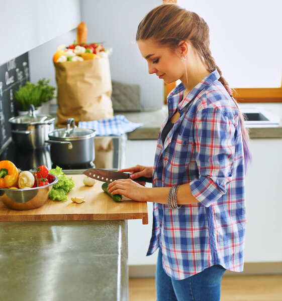 Young woman cutting vegetables in kitchen near desk