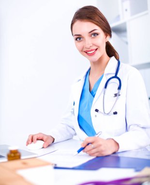 Güzel, genç, gülümseyen bayan doktor masada oturuyor ve yazıyor..