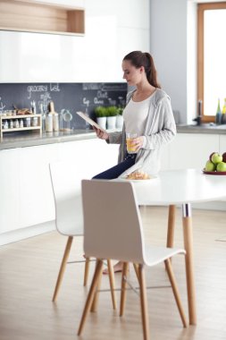 Mutfakta portakal suyu ve tableti olan genç bir kadın..