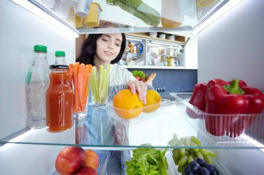 Sağlıklı yiyecek, sebze ve meyvelerle dolu açık buzdolabının yanında duran kadın portresi. Kadın portresi