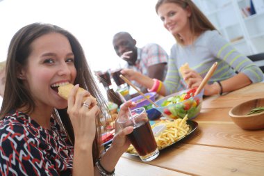 Ahşap masada otururken birlikte yemek yiyen bir grup insanın üst düzey görüntüsü. Masada yemek var. İnsanlar fast food yiyor..
