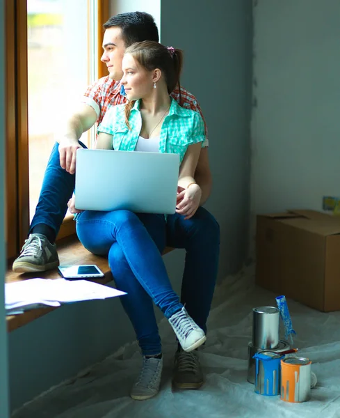 Retrato de pareja joven moviéndose en casa nueva sentado con el ordenador portátil —  Fotos de Stock