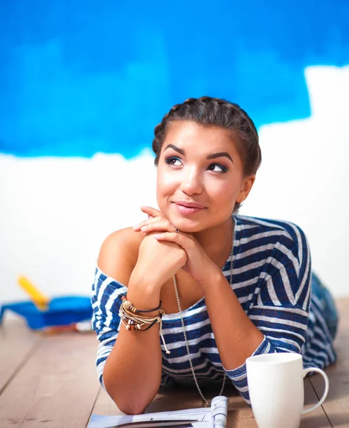 Portrait of female painter lying on floor near wall after paintingand holding a cup — Stock Photo, Image