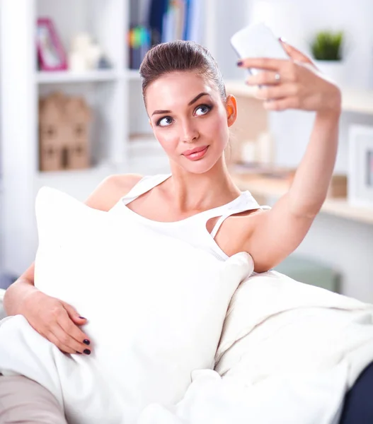 Счастливая брюнетка фотографирует себя со своим мобильным телефоном в спальне — стоковое фото