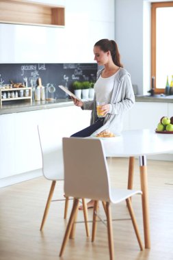 Mutfakta portakal suyu ve tableti olan genç bir kadın..